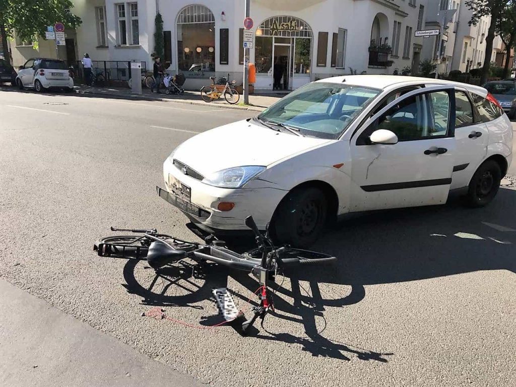 Ein Fahrrad liegt unter einem weißen Auto nach einem Autounfall (Linksabbieger)